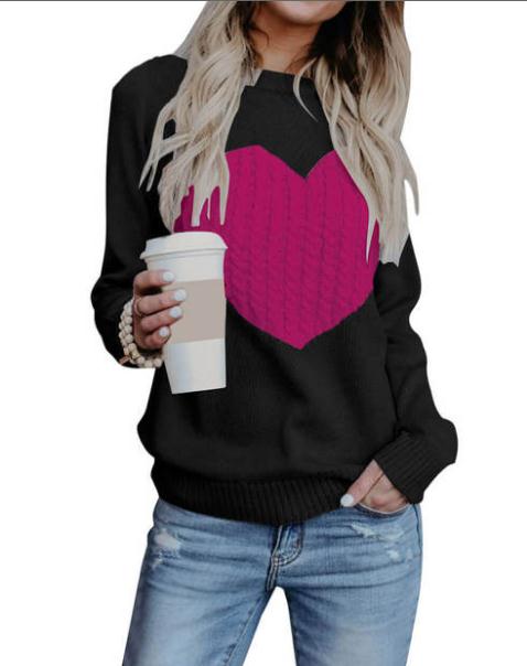 Person wearing a black sweater with a pink heart design, holding a coffee cup.